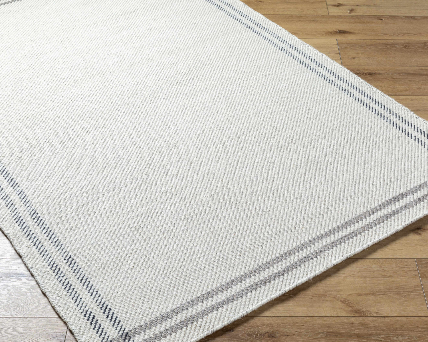Close-up of the hand-woven Nimue Cream & Charcoal Bordered Area Rug showing its wool texture and striped border. Corner