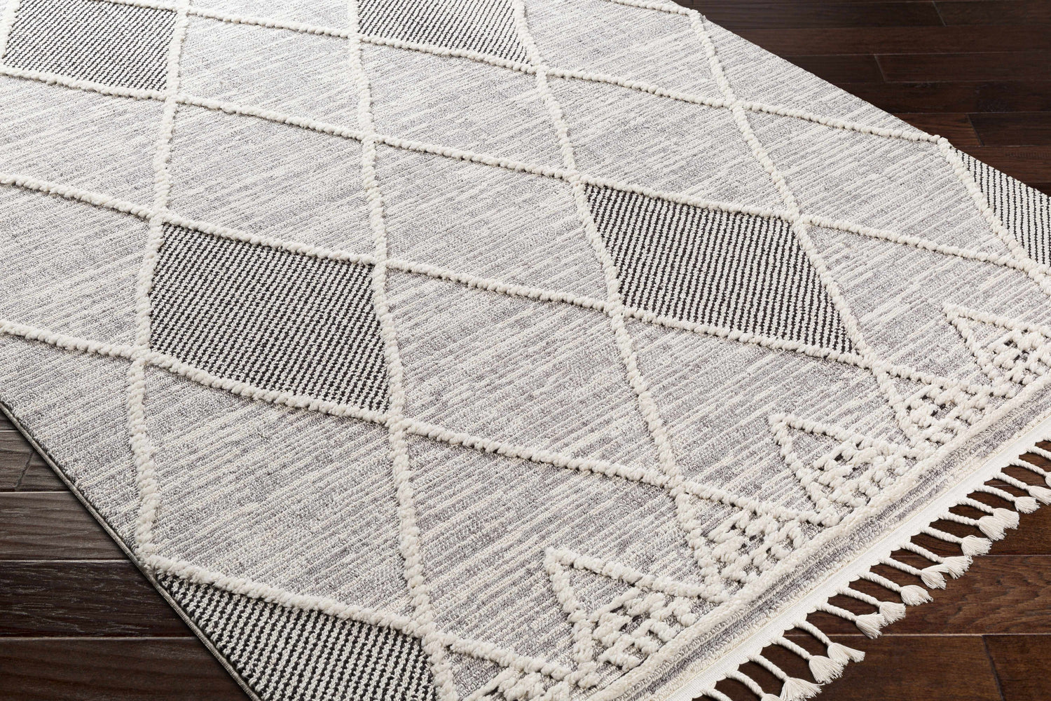 Close-up of the Norvelt rug, a black, gray, and ivory rug with a diamond pattern and tassels. Corner