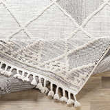 Close-up of the Norvelt High/Low Pile Rug with Tassels, showing its black, gray, and ivory diamond pattern and tassel detail. Fold