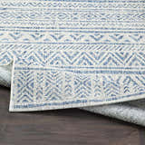 Close-up of the Novato All Over Pattern Performance Rug. Features a blue geometric design on a textured light background. Fold