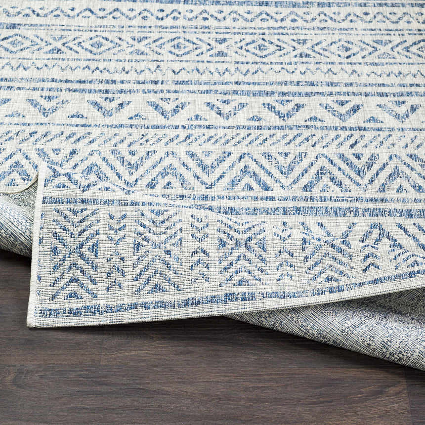 Close-up of the Novato All Over Pattern Performance Rug. Features a blue geometric design on a textured light background. Fold