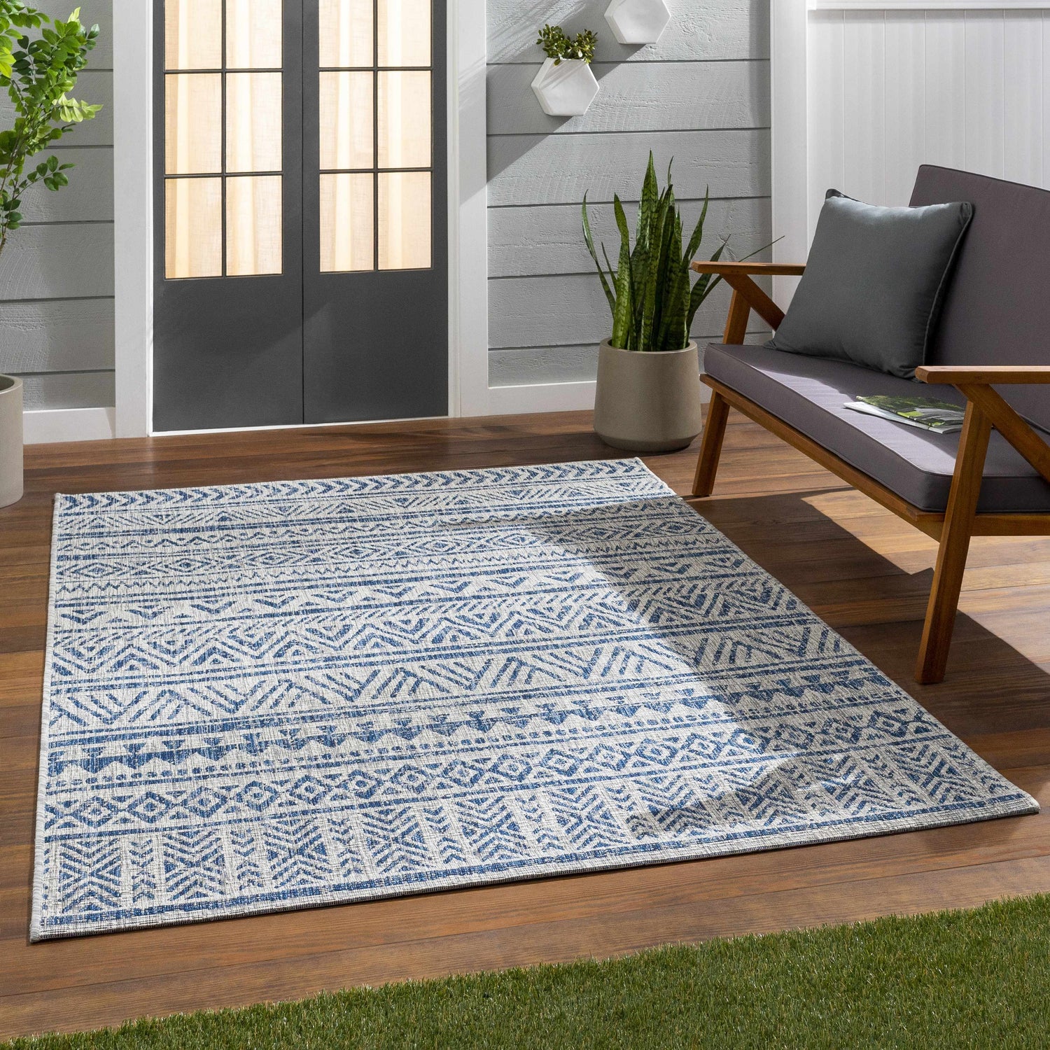 Outdoor patio scene with blue Novato All Over Pattern Performance Rug, gray loveseat, wood floor, and potted plants. Roomscene-Rectangle