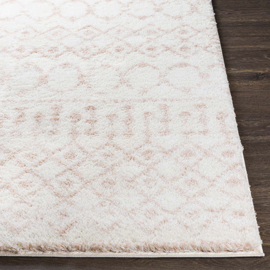 Close-up of the Narrogin Area Rug, a shag rug in cream and blush with a geometric pattern on dark wood flooring. Front