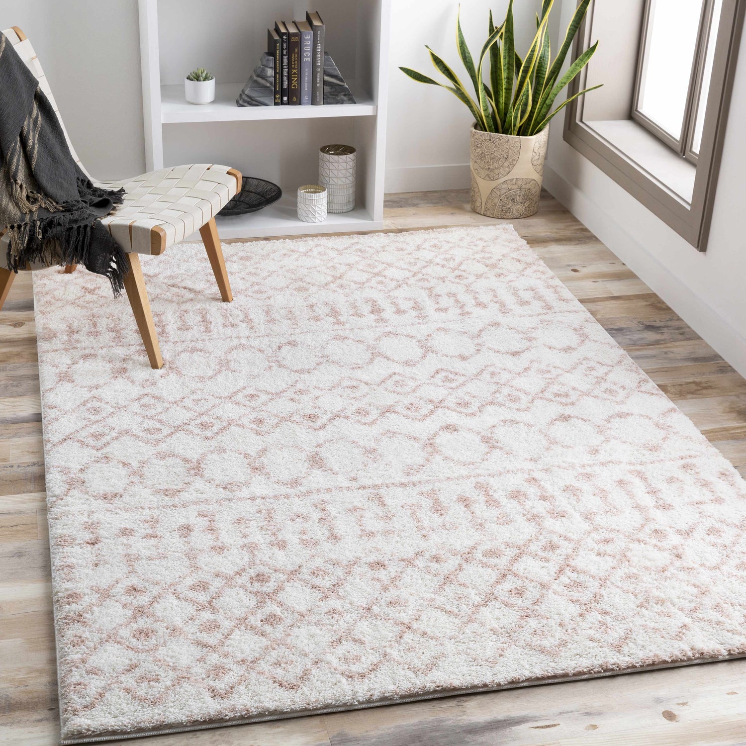 Light and airy room scene with a blush and cream Narrogin Area Rug, woven chair, and white bookshelf. Roomscene-Rectangle