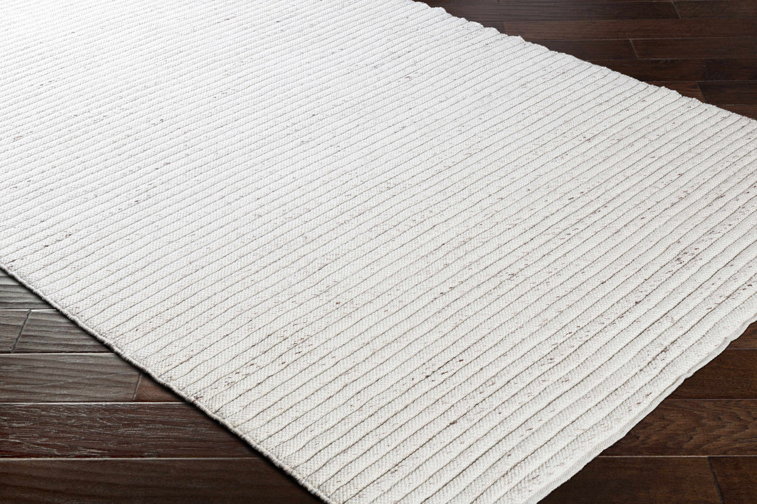 Close-up of the hand woven Nuangola Area Rug. Off white rug with dark brown flecks and a ribbed texture on dark wood flooring. Corner