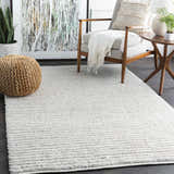 Living room scene with a Nuangola Area Rug in off-white. Features a gray chair, woven pouf, and modern art. Roomscene-Rectangle
