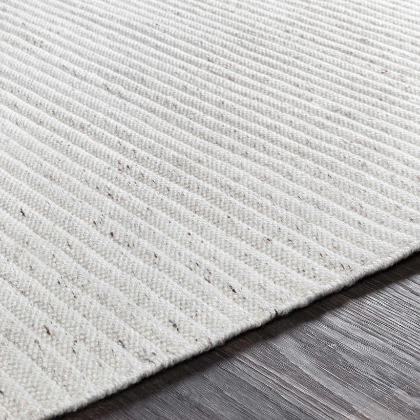 Close-up of the hand-woven Nuangola Area Rug. Off-white polyester rug with subtle dark brown specks and a textured, ribbed design. Texture