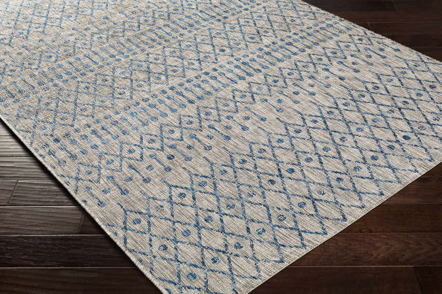 Close-up of Newbern Outdoor Rug. Blue geometric pattern on taupe background. Machine woven polypropylene rug. Corner