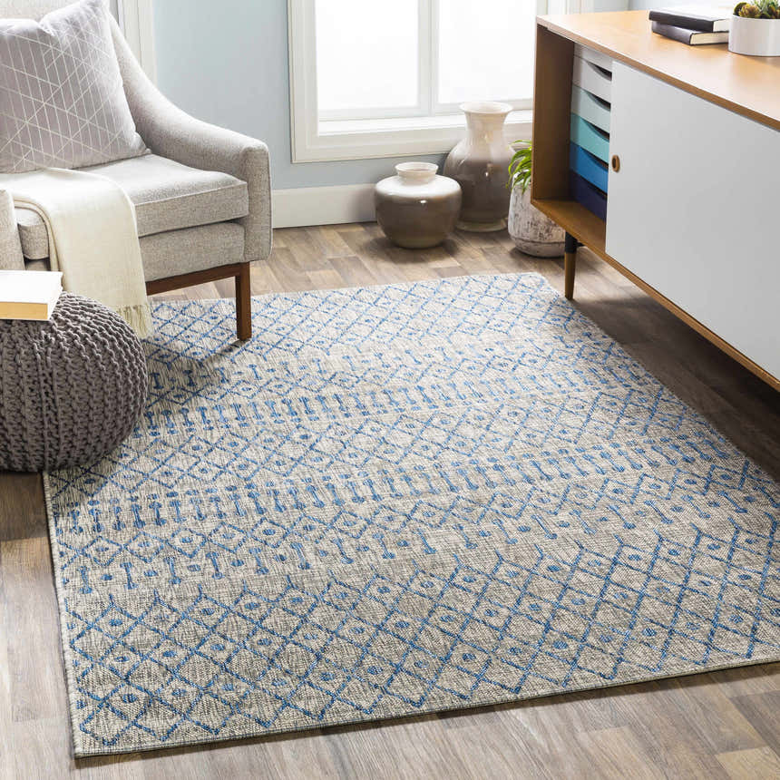 Living room scene with blue and taupe Newbern Outdoor Rug, gray chair, and modern cabinet. Roomscene-Rectangle