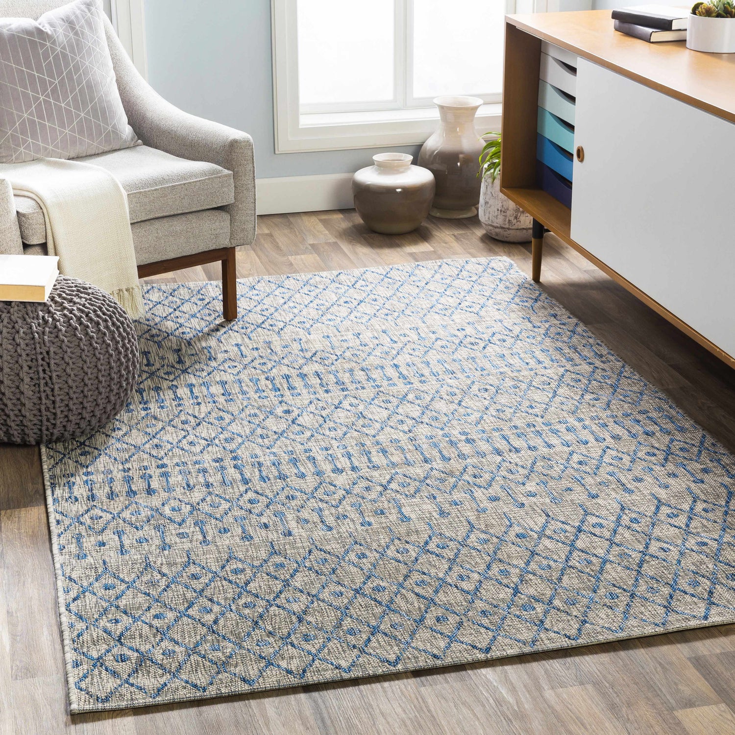 Living room scene with blue and taupe Newbern Outdoor Rug, gray chair, and modern cabinet. Roomscene-Rectangle