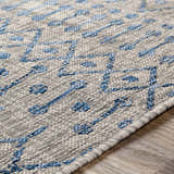Close-up of Newbern Outdoor Rug featuring a blue geometric pattern on a textured taupe background. Texture