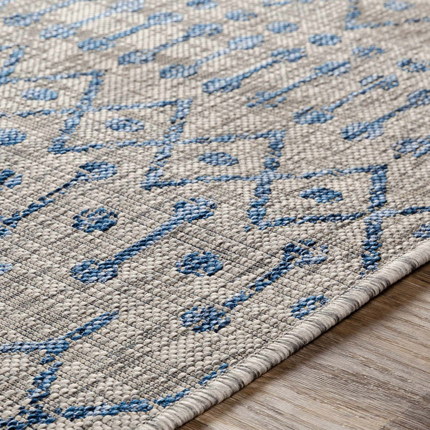 Close-up of Newbern Outdoor Rug featuring a blue geometric pattern on a textured taupe background. Texture