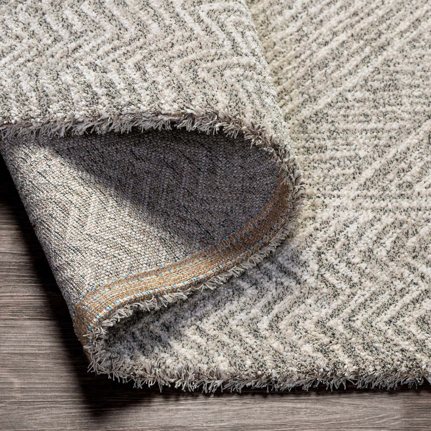 Close-up of the Nyngan Luxe Rug showing its light beige, gray, and black contemporary herringbone pattern and textured weave. Fold