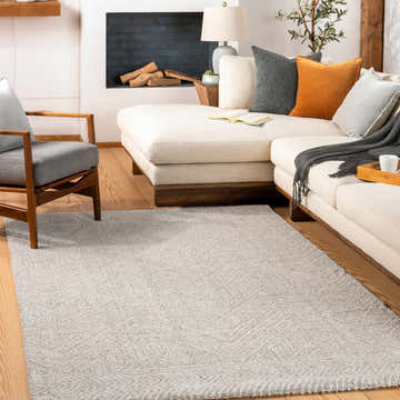 Living room scene with a light beige Nyngan Luxe Rug, white sectional sofa, gray chair, and wood floors. Roomscene-Rectangle