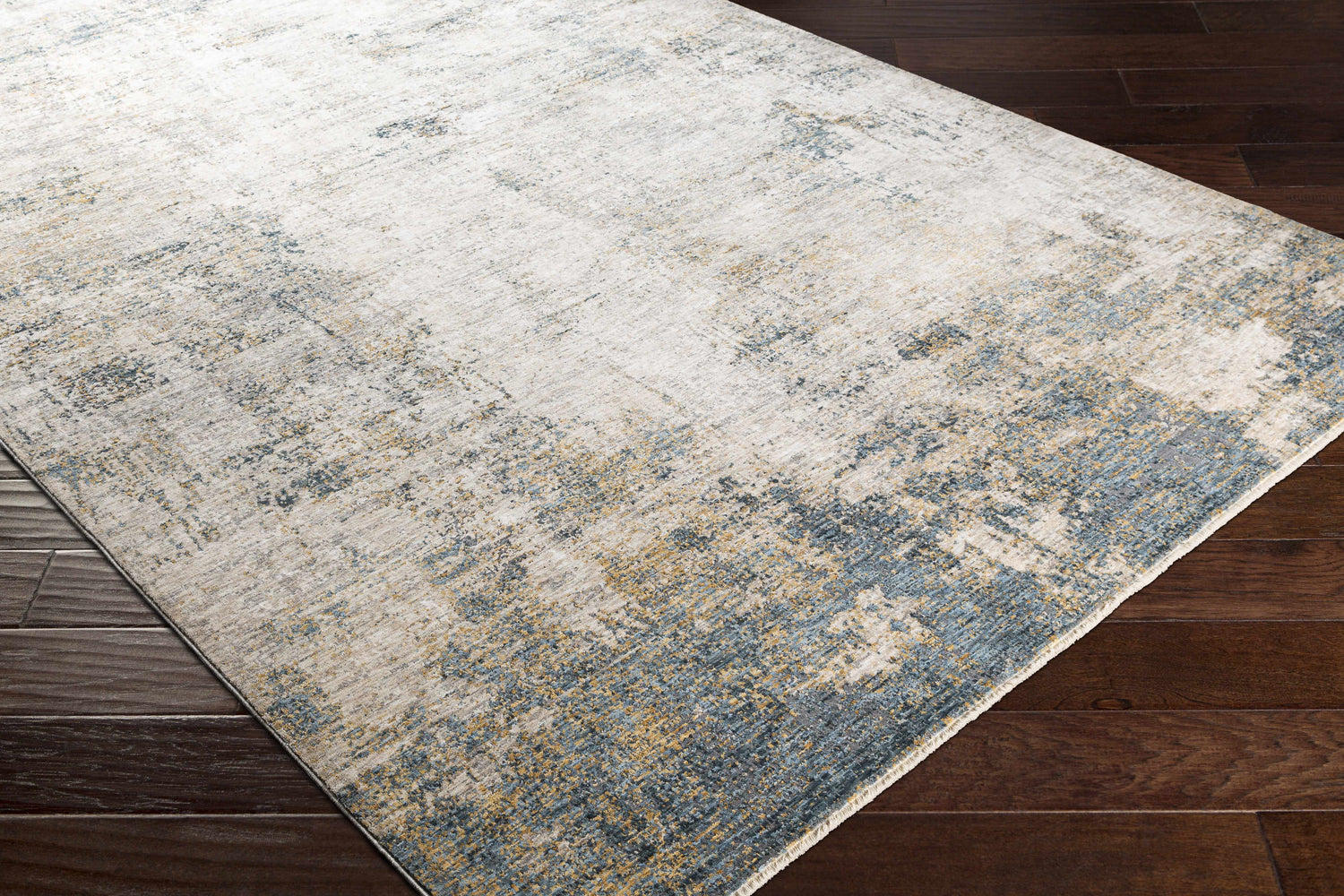 Close-up of the Odell Abstract Luxe Fringe Rug in dark blue, light blue, gray, and mustard on a dark wood floor. Corner
