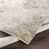 Close-up of the Odell Abstract Luxe Fringe Rug, featuring dark blue, light blue, gray, and mustard colors. Fold