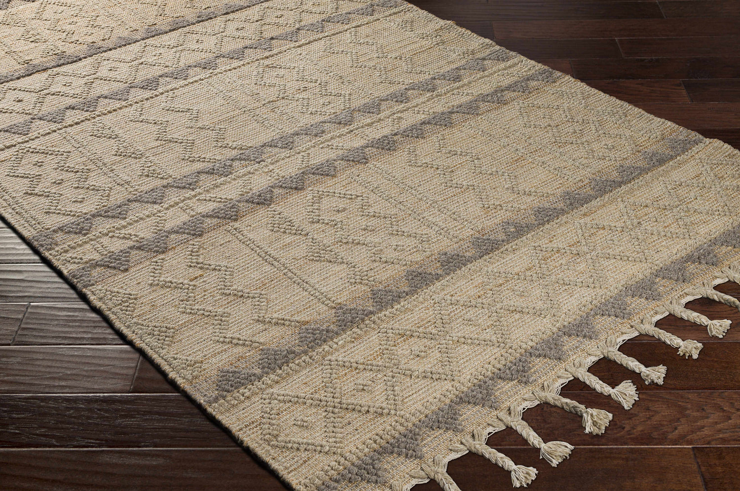 Close-up of the Okurcalar Area Carpet. Tan and gray jute-wool rug with a geometric pattern and braided tassels. Corner