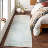 Bedroom scene with a light beige and teal Omega Area Rug, wood floors, and a bed with neutral bedding. Roomscene-Runner