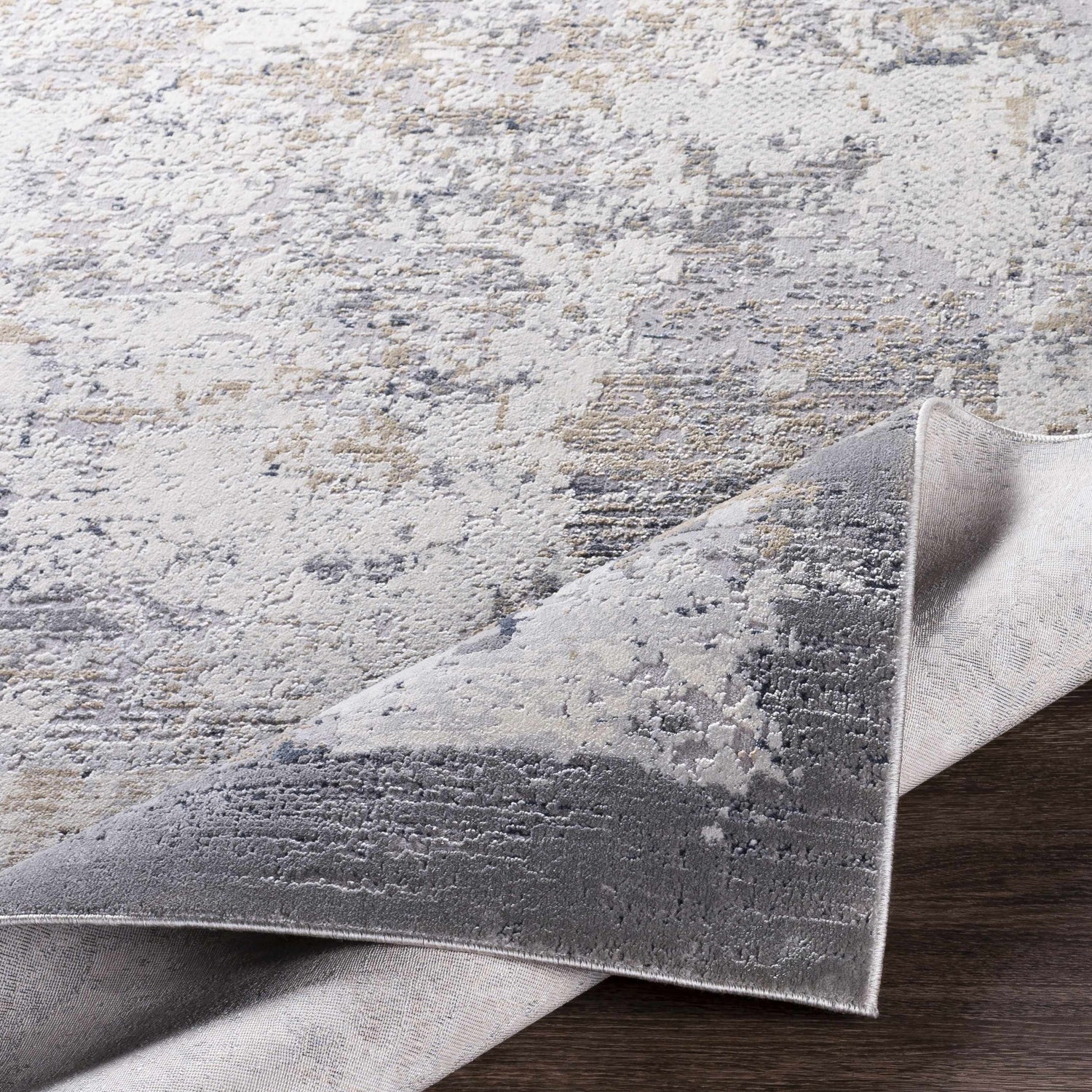 Close-up of the Ooralea Area Rug showing its charcoal, beige, and gray contemporary pattern and machine-woven construction. Fold