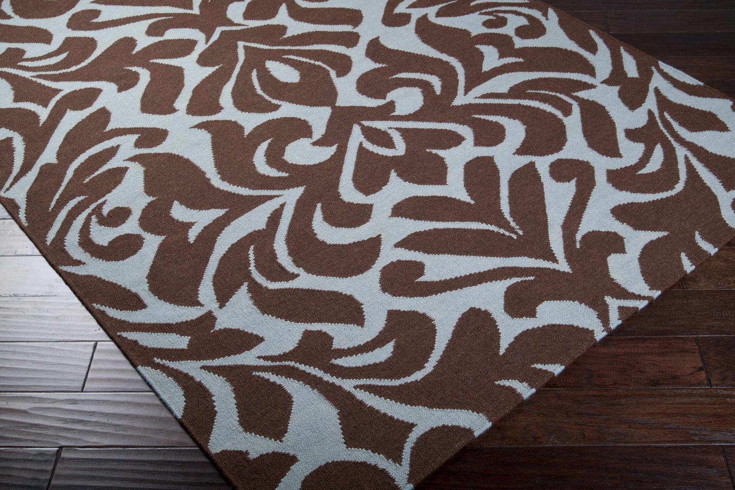 Close up of the Oppelo Area Rug, a hand woven wool rug in dark brown and sage with a contemporary floral pattern. Corner