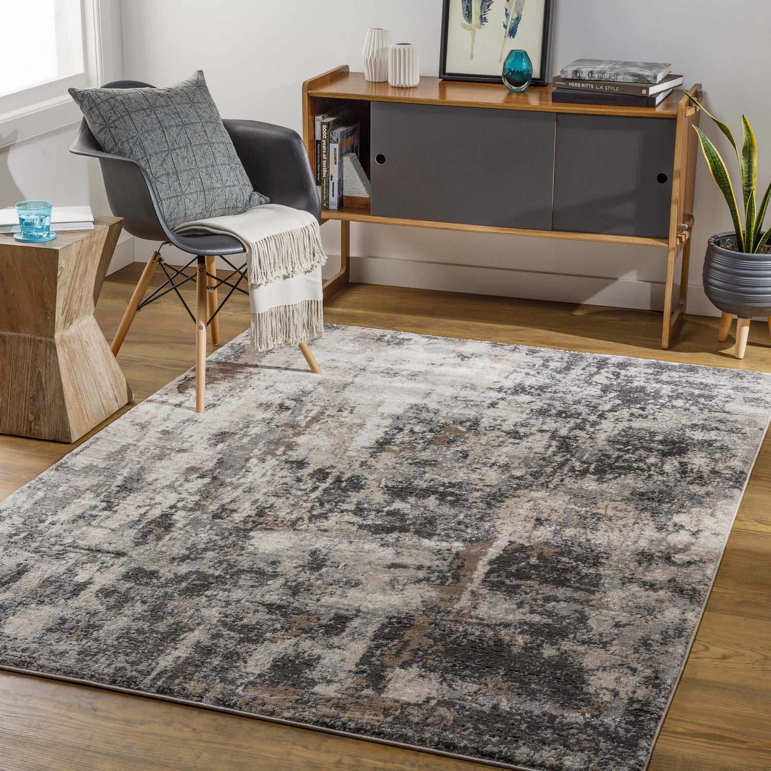 Living room scene with a gray chair, wood cabinet, and Opunake Luxe Area Rug in black, brown, charcoal, cream, gray, and tan. Roomscene-Rectangle
