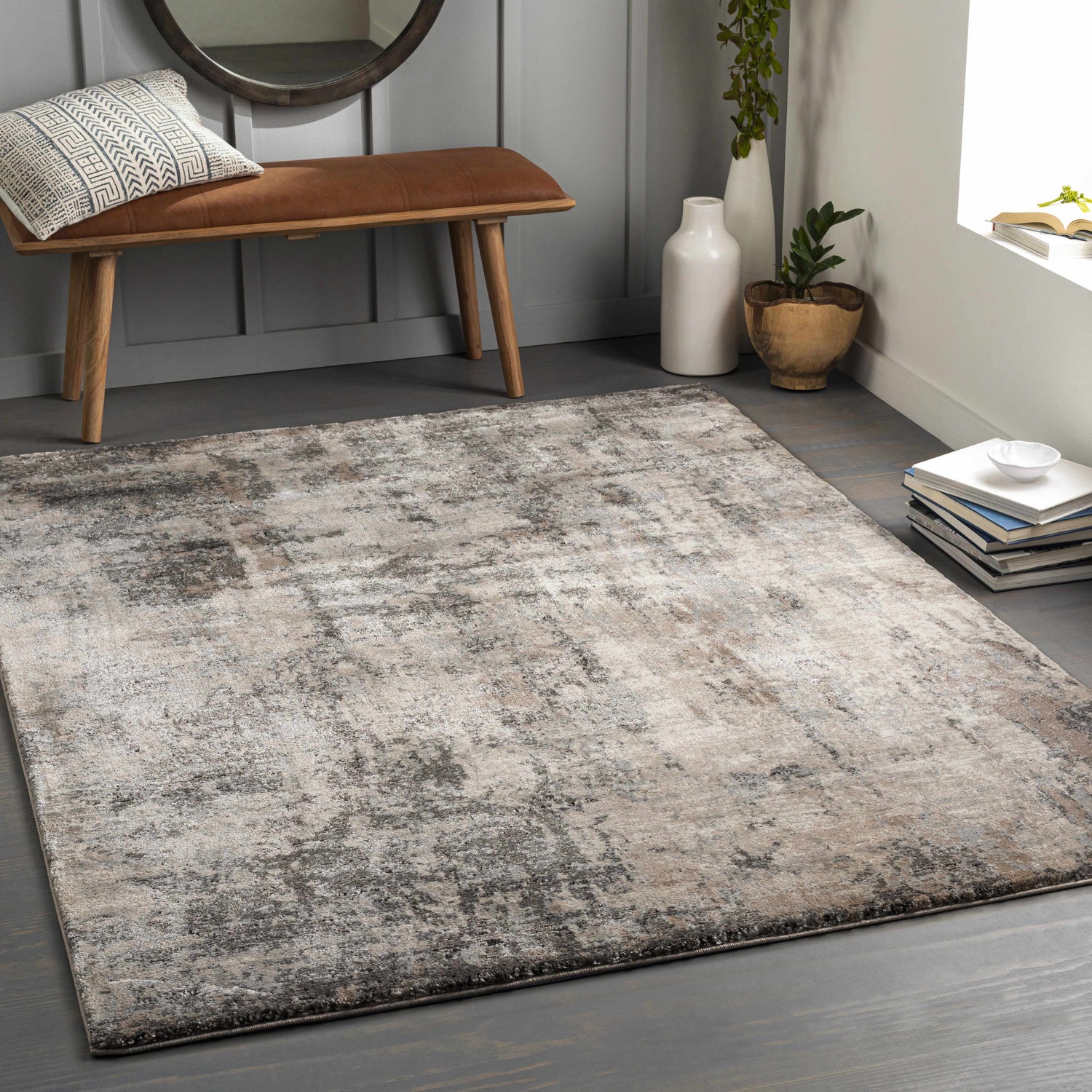 Contemporary living room scene with Opunake Luxe Thick Area Rug in black, brown, cream, and gray tones. Bench, mirror, and plants. Roomscene-Rectangle
