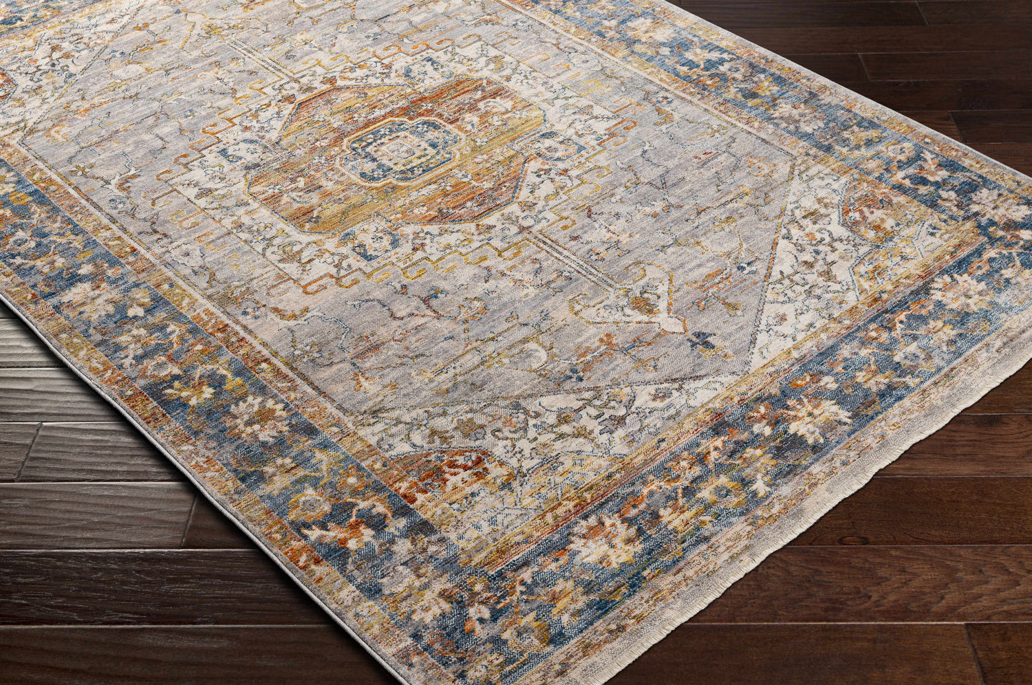 Close-up of Orchards Area Rug: Bohemian-style rug in brick red, burnt orange, cream, and blue on dark hardwood floors. Corner