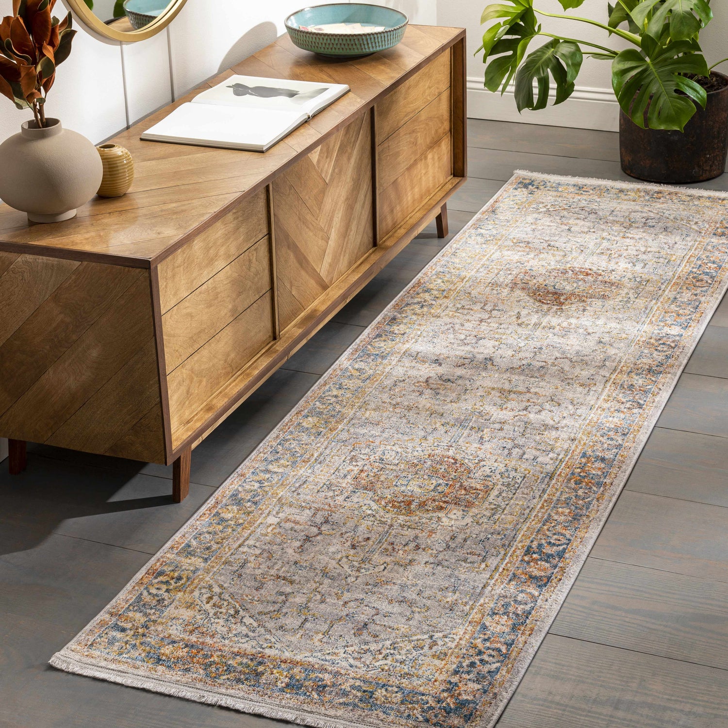 Hallway scene with Orchards Area Rug runner in brick red, burnt orange, blue, and gray. Bohemian style with wood console table and monstera plant. Roomscene-Runner