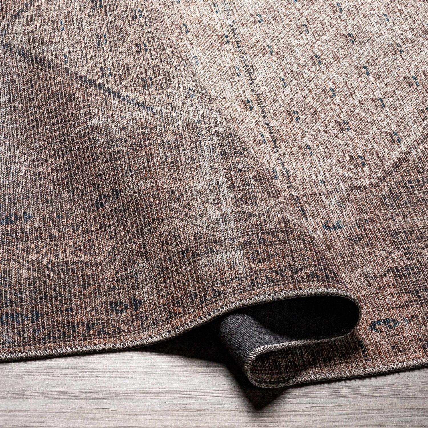 Close-up of the Tan Ormstown Distressed Washable Area Rug showing its tan, brown, and blue traditional design and texture. Fold