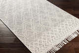 Close-up of the Ossun Wool Rug. Cream rug with geometric pattern and tassels on dark wood floor. Corner