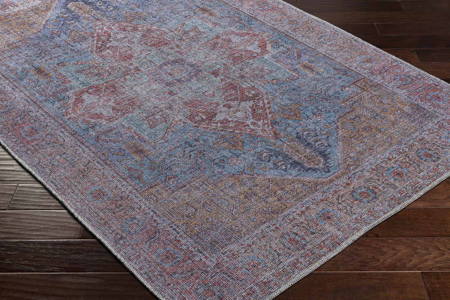 Close-up of the Otaki Washable Area Rug showing its traditional oriental pattern in dark gray, purple, brown, and natural gray tones. Corner