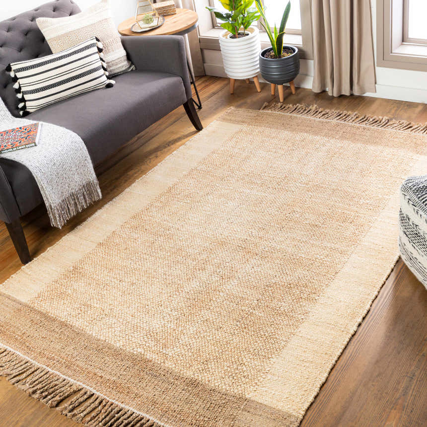 Living room scene with a tan Outaouais Jute Rug, gray sofa with throw pillows, plants, and wood floors. Roomscene-Rectangle