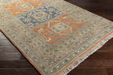 Close-up of the Overstrand Area Rug. Hand-knotted wool rug with burnt orange, dark blue, and green traditional pattern. Corner