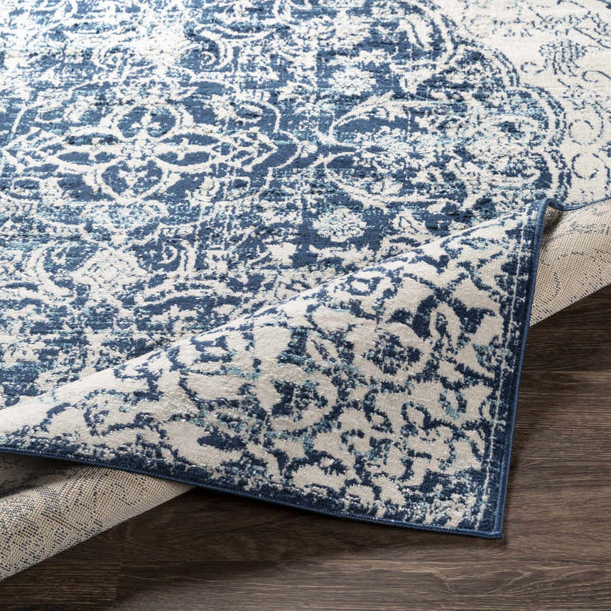 Close-up of Pannal Area Rug showing its light beige and navy bohemian pattern and texture on dark wood floor. Fold