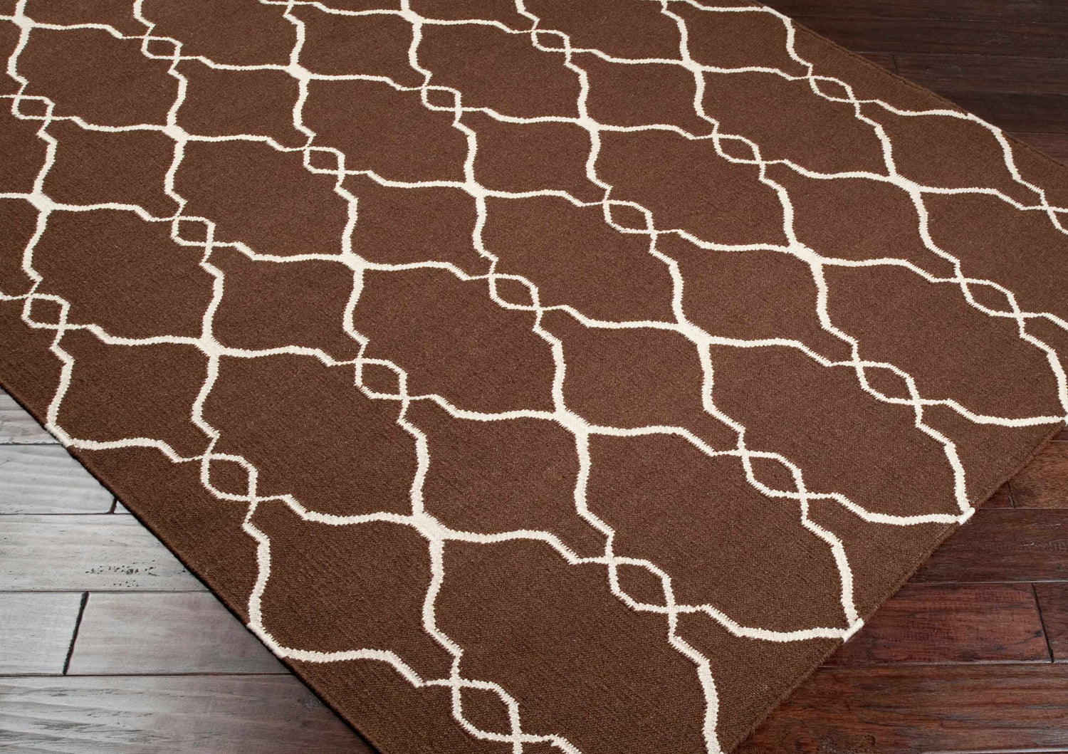 Close-up of Partington Brown Wool Carpet Area Rug featuring a geometric trellis pattern in beige on a dark brown background. Corner