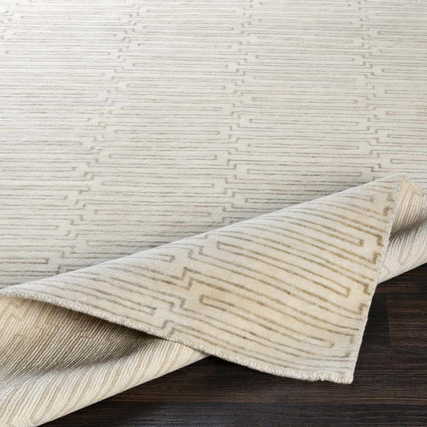 Close-up of the Partlow Area Rug, a beige and cream hand-knotted rug with a contemporary geometric pattern. Fold