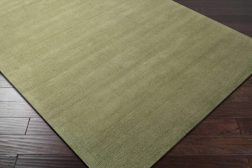 Close-up of the Brockton Solid Green hand-loomed wool rug showing its sage color and subtle striped texture on dark wood floors. Corner