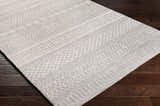 Close-up of the Pewsey Tribal Area Rug. Cream and gray rug with hand-hooked tribal patterns on dark wood floor. Corner
