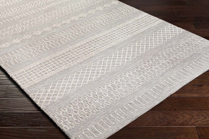 Close-up of the Pewsey Tribal Area Rug. Cream and gray rug with hand-hooked tribal patterns on dark wood floor. Corner