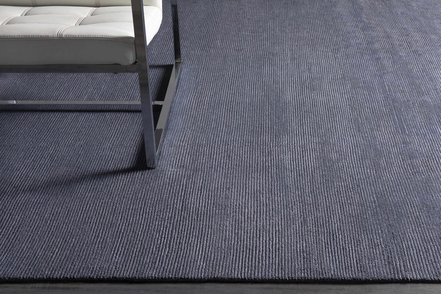 Close-up of Philipsburg Carpet in dark blue with a subtle striped texture and a modern white chair. Styleshot