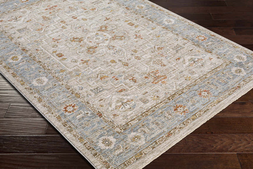 Close-up of the Phyllis Thick Luxe Statement Rug showing its beige, blue, and rust traditional pattern on dark wood floors. Corner