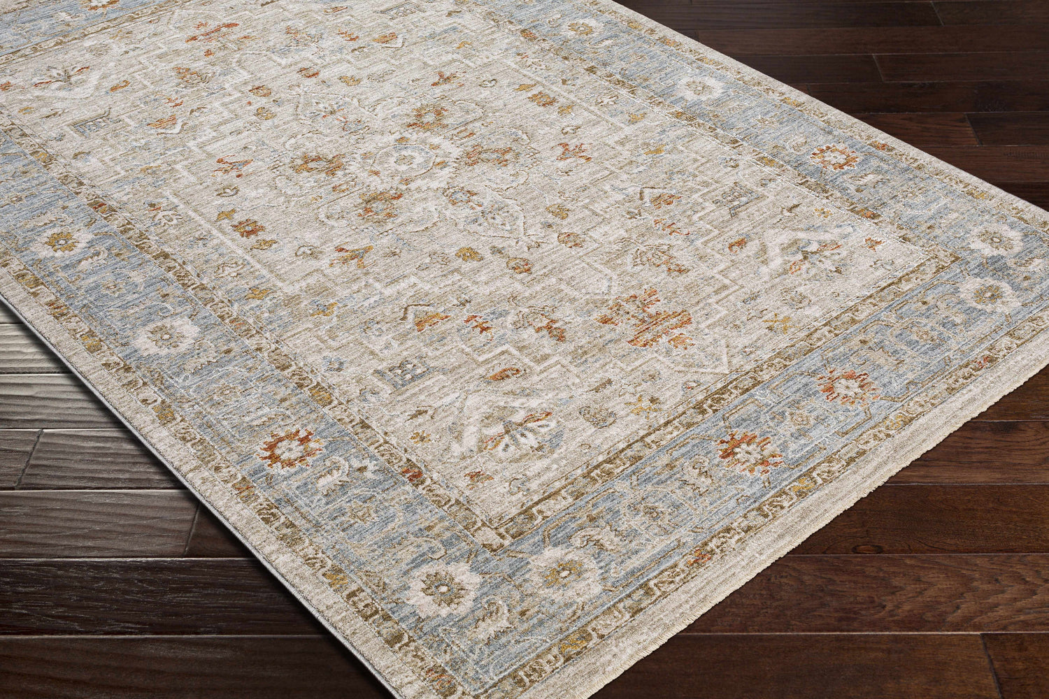 Close-up of the Phyllis Thick Luxe Statement Rug showing its beige, blue, and rust traditional pattern on dark wood floors. Corner