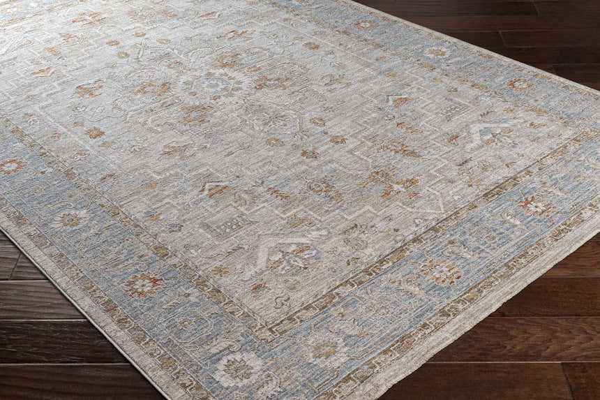 Close-up of the Phyllis Thick Luxe Statement Rug, showcasing its light beige, blue, and brick red traditional pattern. Corner