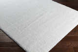 Close up of a white Piedmont Area Rug, a shag rug made of polyester on dark wood flooring. Corner