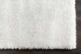 Close-up of a plush white Piedmont Area Rug with a shag texture on a dark wood floor. Corner
