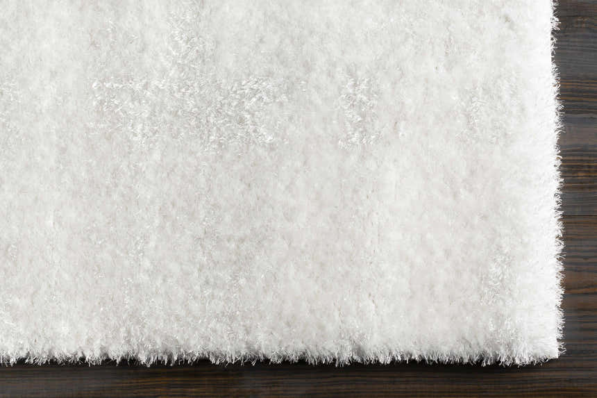 Close-up of a plush white Piedmont Area Rug with a shag texture on a dark wood floor. Corner