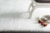 Close-up of the white Piedmont Area Rug, a shag rug with a soft texture, styled with a chair and decorative plates. Styleshot