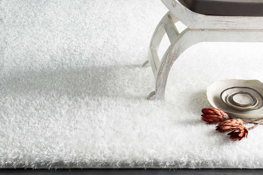 Close-up of the white Piedmont Area Rug, a shag rug with a soft texture, styled with a chair and decorative plates. Styleshot