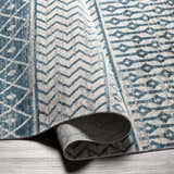 Close-up of the Pinamopoan Washable Area Rug. Features a contemporary geometric pattern in light beige and blue hues. Fold