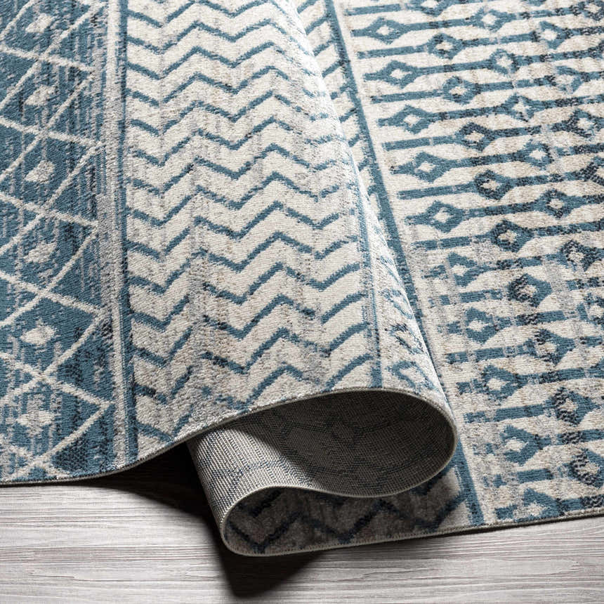Close-up of the Pinamopoan Washable Area Rug. Features a contemporary geometric pattern in light beige and blue hues. Fold